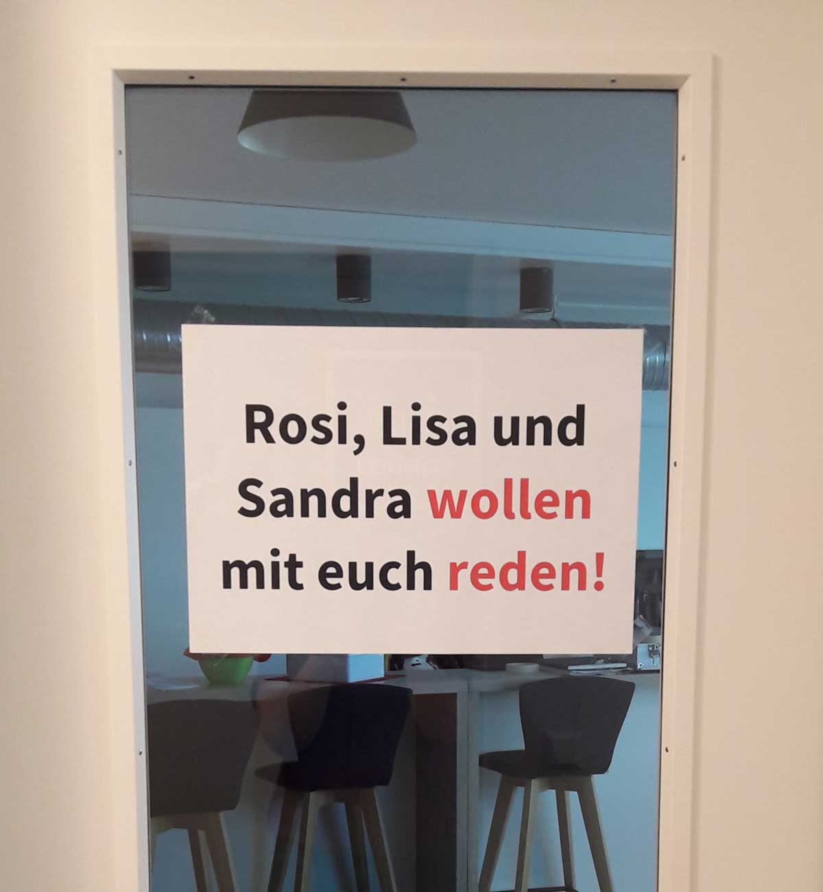 Bild zeigt ein Türschild mit der Aufschrift "Rosi, Lisa und Sandra wollen mit euch reden!", welches zum Nachbarschaftsgespräch einlädt.